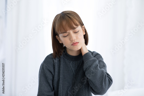 young Asian woman sitting on bed has neck pain after wake up in the morning,Healthcare Concept