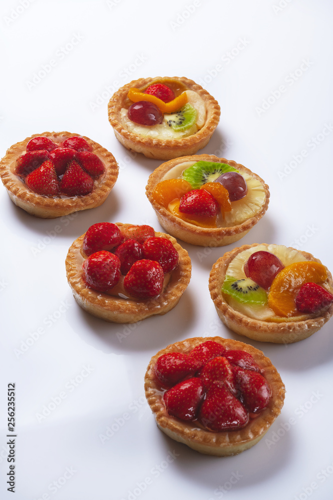 Basket-cakes with mascarpone cheese and decorated with different fruit on white plate. High Key. Close up. Selective focus. Top view.
