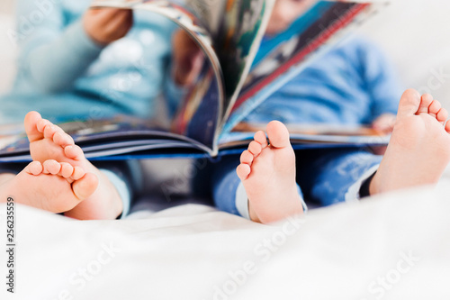 Two children friend reading a book on a white bed. Kids toes