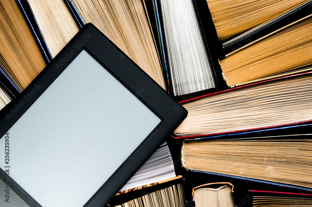 Fototapeta premium The e-book with a white screen lies on the open multi-colored books that lie on a dark background, close-up