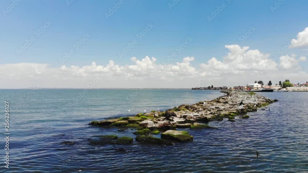 Summer landscape with Seagull perched on pier with bright sky and cove behind, aerial view, drone. Ocean cove with blue sky and clouds, bird's-eye view Summer landscape with Seagull perched on pier with bright sky and cove behind, aerial view, drone. Ocean cove with blue sky and clouds, bird's-eye view