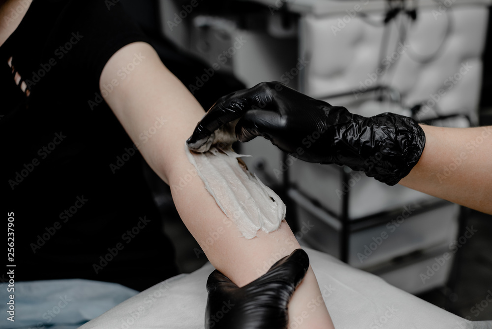 depilation and beauty concept - sugar paste or wax honey for hair removing with black gloves hands of cosmetologist in spa salon