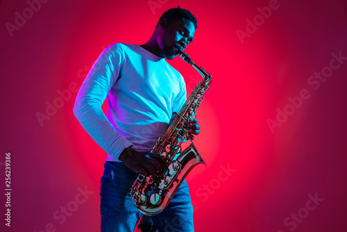 Photography African American handsome jazz musician playing the saxophone in the studio on a neon background