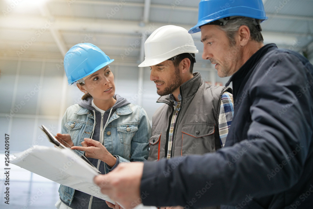Team of construction workers talking in empty warehouse Team of construction workers talking in empty warehouse