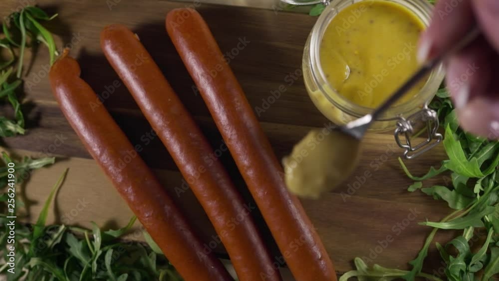 Chef pours spicy mustard sauce to the smoked sausages in slow motion, smoked meat and beer snacks, fast food barbeque sausage, grilled meat, semifinished food, Full HD 60fps