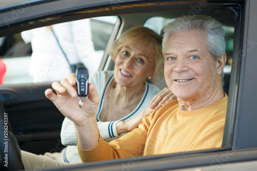 Happy elderly couple holding car key to their new automobile