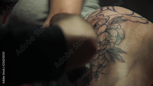 tattoo master in black shirt cleans pigment from part of big flower tattoo on young girl left thigh and smears salve