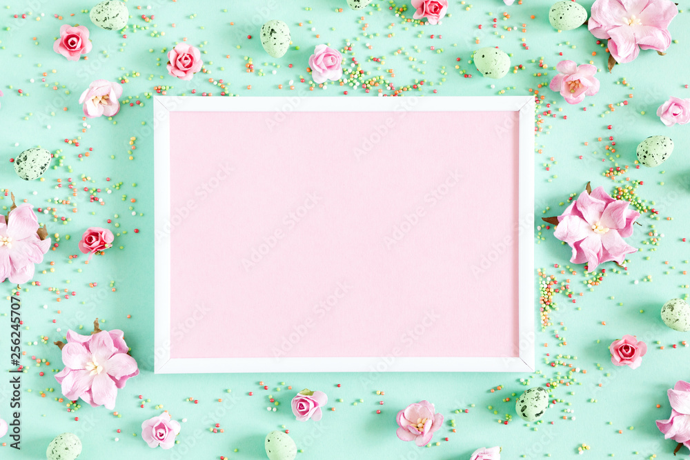 Easter decor, composition. Blank photo frame, flowers, easter eggs on pastel mint background. Flat lay, top view, copy space