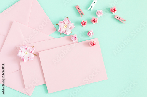 Flowers composition romantic. Pink envelopes and flowers on pastel mint background. Flat lay, top view, copy space