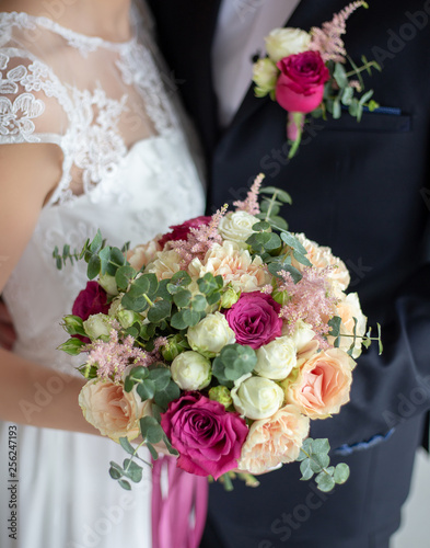 Closeup view of beautiful floral decor made of fresh pastel colors flowers. Happy young bride and groom standing together. Color photography.