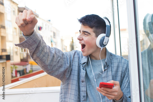 young euphoric with mobile phone and headphones celebrating success