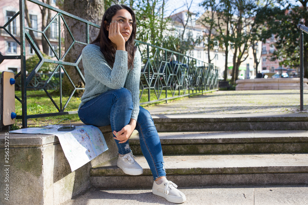 Dreamy pretty young woman sitting on city stairs parapet