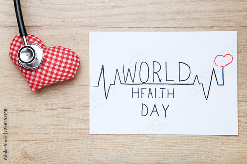Text World Health Day with stethoscope and fabric heart on wooden table