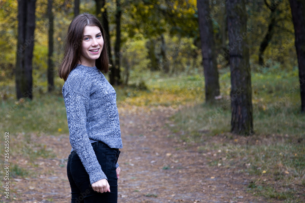 cute girl in a gray sweater is half a turn on the road in the autumn forest. Copy space area cute girl in a gray sweater is half a turn on the road in the autumn forest. Copy space area