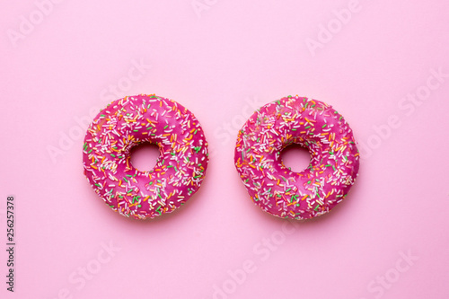 Sweet pink donuts with multicolored sprinkles on a pink background flat lay