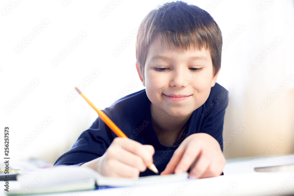 Portrait cute, cheerful little boy in a bright room. Child writing in a notebook with a pencil. Preteen schoolboy doing his homework. Portrait cute, cheerful little boy in a bright room. Child writing in a notebook with a pencil. Preteen schoolboy doing his homework.