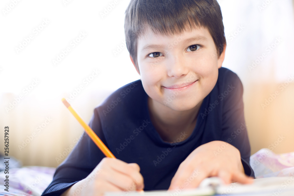 Portrait cute, cheerful little boy in a bright room. Child writing in a notebook with a pencil. Preteen schoolboy doing his homework. Portrait cute, cheerful little boy in a bright room. Child writing in a notebook with a pencil. Preteen schoolboy doing his homework.
