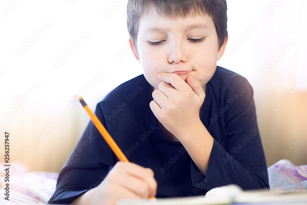 Portrait cute, cheerful little boy in a bright room. Child writing in a notebook with a pencil. Preteen schoolboy doing his homework. Portrait cute, cheerful little boy in a bright room. Child writing in a notebook with a pencil. Preteen schoolboy doing his homework.