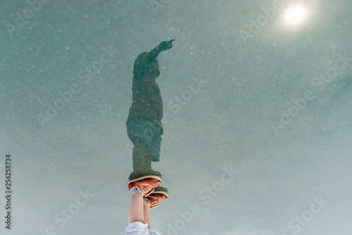 Reflection of boy with hand raised standing in puddle