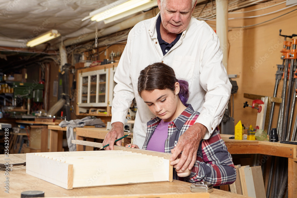Carpenter assisting girl in making wooden shelf