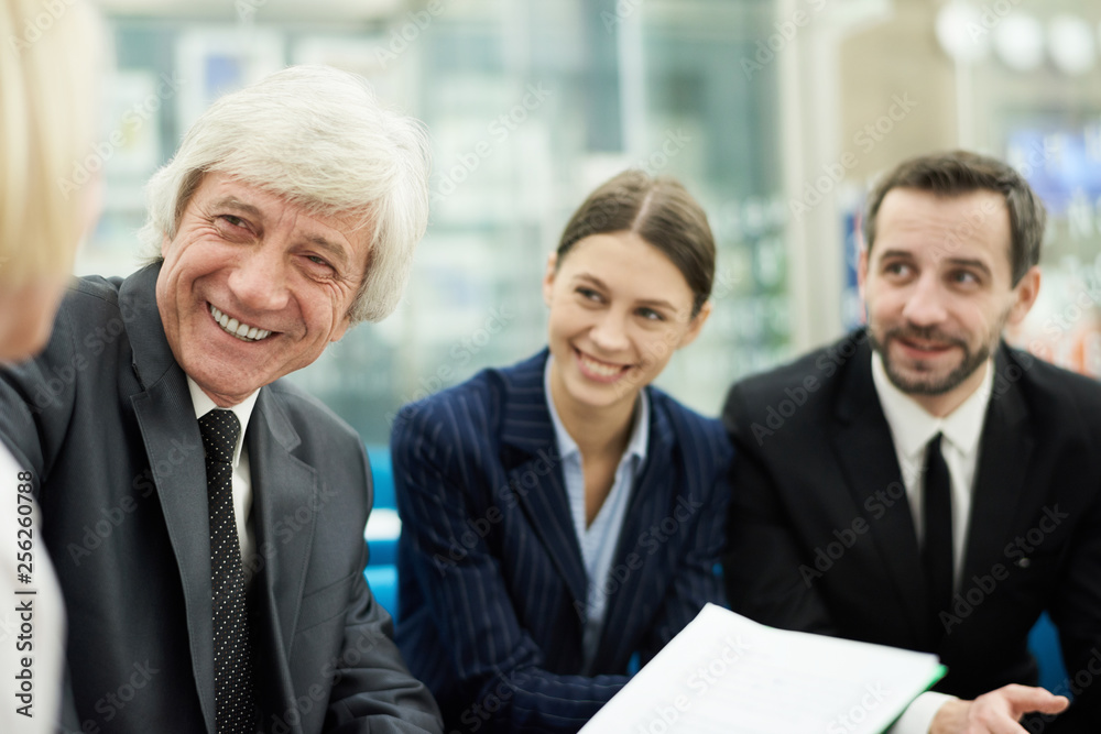 Group of business people discussing project in meeting, focus on smiling senior businessman in foreground, copy space Group of business people discussing project in meeting, focus on smiling senior businessman in foreground, copy space