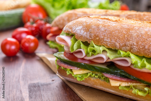 Long Baguette Sandwich with lettuce, slices of fresh tomatoes, ham, turkey breast and cheese