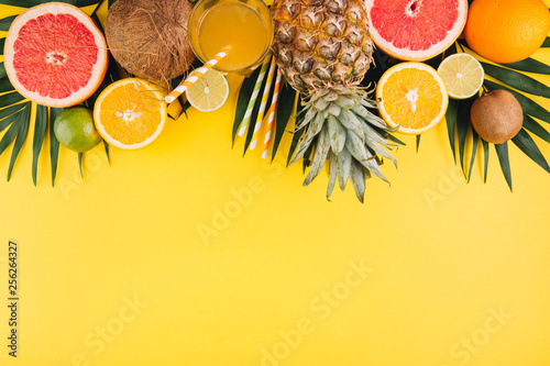 Summer fruits. Tropical palm leaves, pineapple, coconut, grapefruit, orange and glass of juice on yellow background. Flat lay, top view, copy space photo