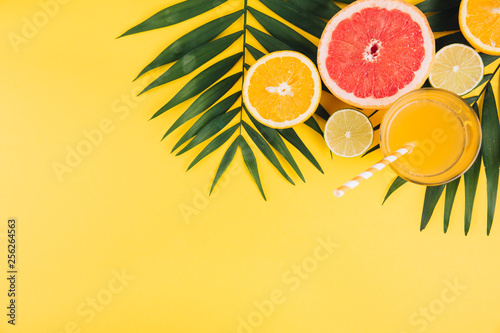 Fototapeta Naklejka Na Ścianę i Meble -  Summer fruits. Tropical palm leaves, lime, grapefruit, orange and glass of juice on yellow background. Flat lay, top view, copy space