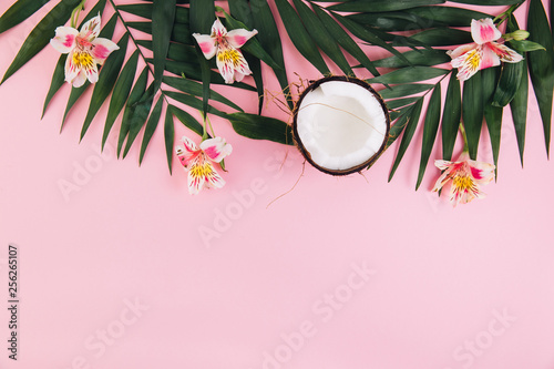 Coconut, flowers astroemeria and palm leaves on a pink background photo