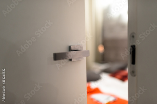  Ajar door to a modern bedroom with a light, visible blurred bed, bedding and orange pillows. photo