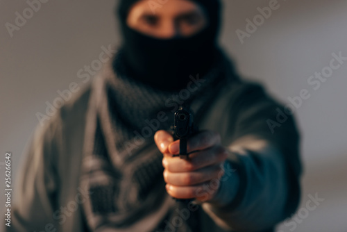 Terrorist in mask and scarf aiming gun at camera photo