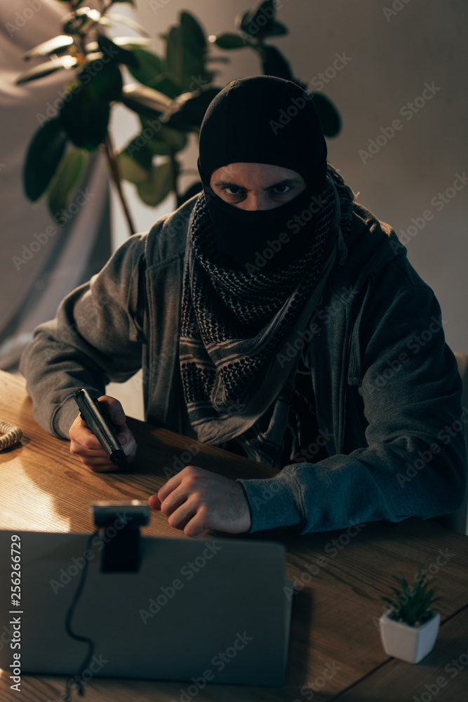Angry terrorist in mask aiming gun and looking at camera Angry terrorist in mask aiming gun and looking at camera