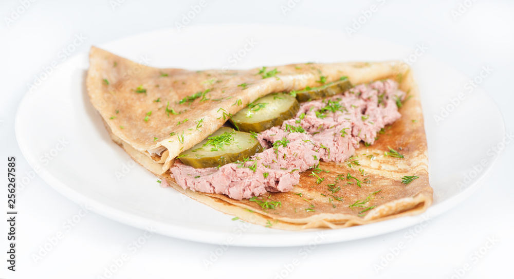Thin delicious pancake with meat pate and cucumber on white