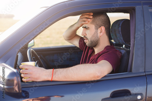 Frightened terrified dark haired unshaved man, stops his car on side of road, drinks tea, sees with shock through windshield at accident, being very emotional, keeps hand on forehead. Safety concept.