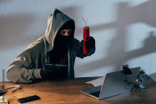 Terrorist in black mask with dynamite aiming gun at webcam photo