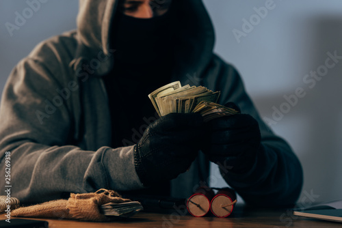 Partial view of terrorist in mask counting dollar banknotes photo