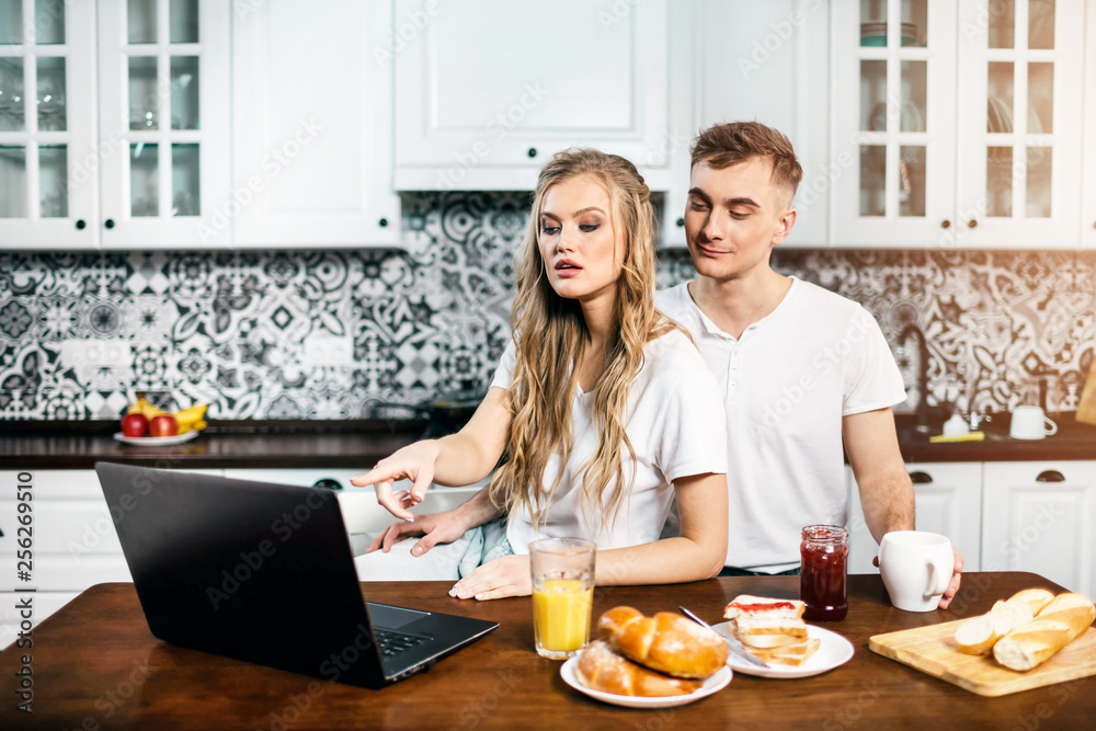Amazing couple using laptop together in the light kitchen at home