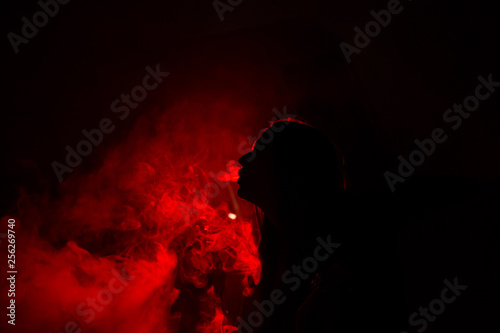 Girl model smokes vape in red light.