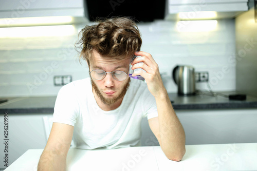 bearded male alcoholic man drinks alcohol from a glass at home in the kitchen. The concept of a hangover and alcoholism