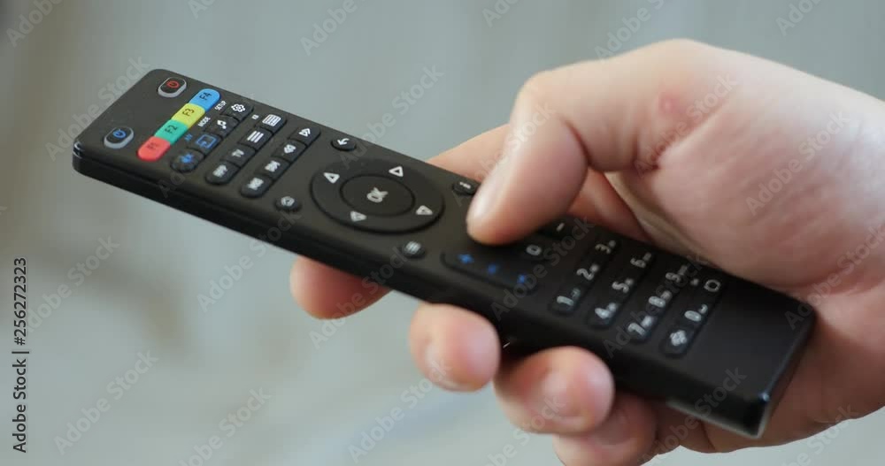 Close up mans hand holding TV remote control and changing TV channels Close up mans hand holding TV remote control and changing TV channels