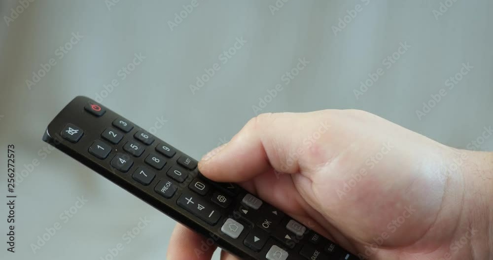 Close up mans hand holding TV remote control and changing TV channels Close up mans hand holding TV remote control and changing TV channels