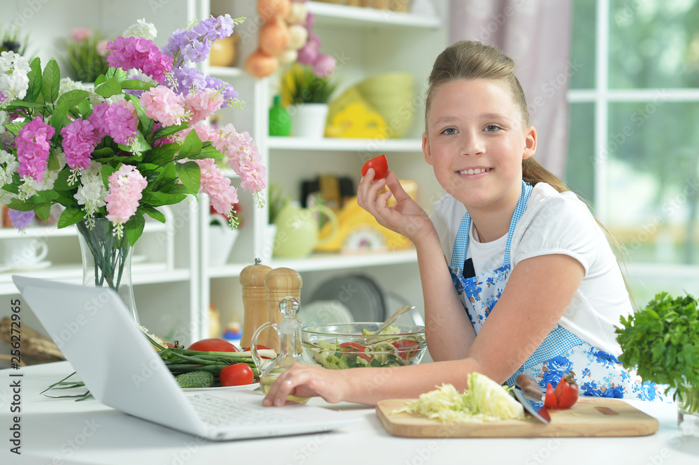 Portrait of cute teen girl using laptop while preparing fresh salad on kitchen table Portrait of cute teen girl using laptop while preparing fresh salad on kitchen table
