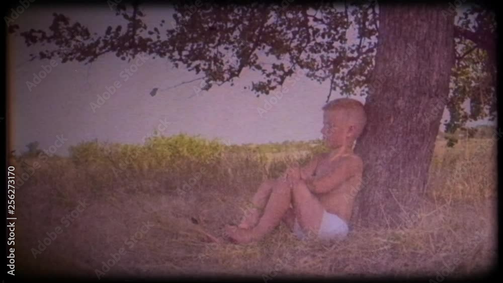 Family video archive. Retro camera 8 mm. Vintage. A little boy sits and dreams under a big tree. Childhood dreams. Place of solitude. Journey back to childhood. Fabulous tree. Memories.  A warm wind
