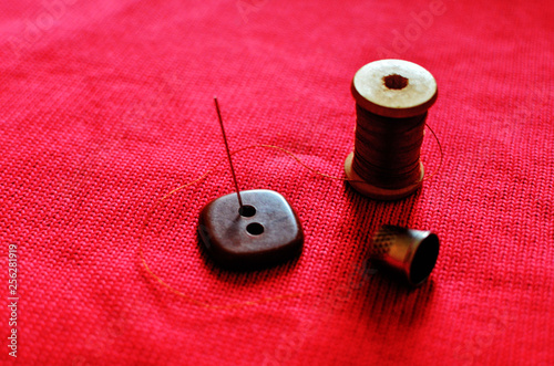 Accessories for sewing and darning clothes: needle, thread, button and thimble on a red background of wool fabric