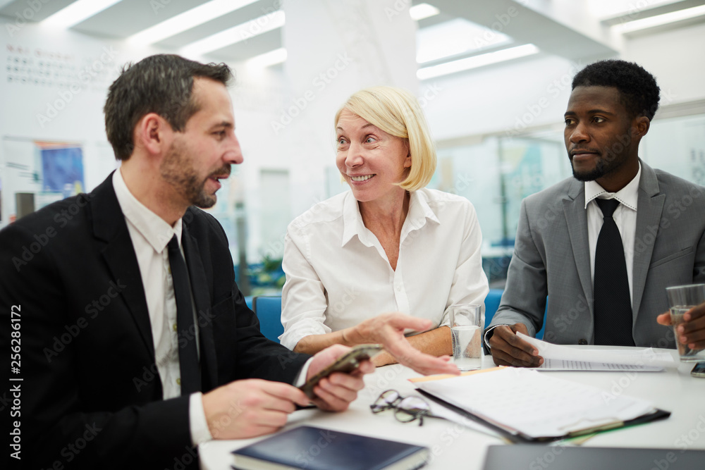 Multi-ethnic group of people sitting at table during meeting in office, focus on smiling female boss in center Multi-ethnic group of people sitting at table during meeting in office, focus on smiling female boss in center