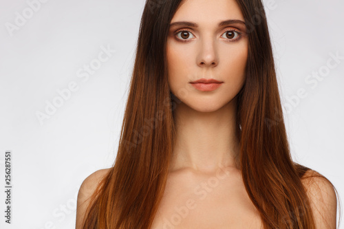 Portrait of a beautiful woman with straight long hair and interesting emotion. Light gray background