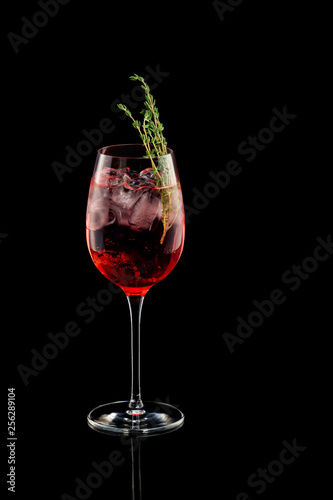Glass of red sangria wine cocktail decorated with thyme isolated at black background.