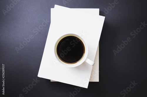 Black coffee in a white coffee mug placed on white books stacked on a black background