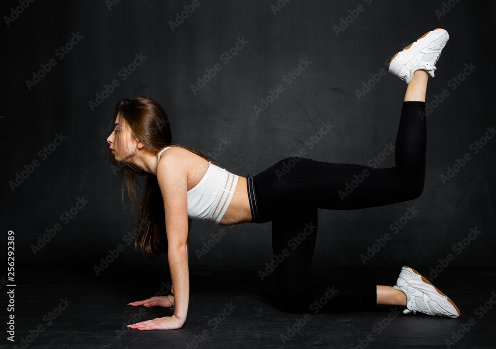 Athletic and strong young woman doing some exercise on a black background. Stretching exercises