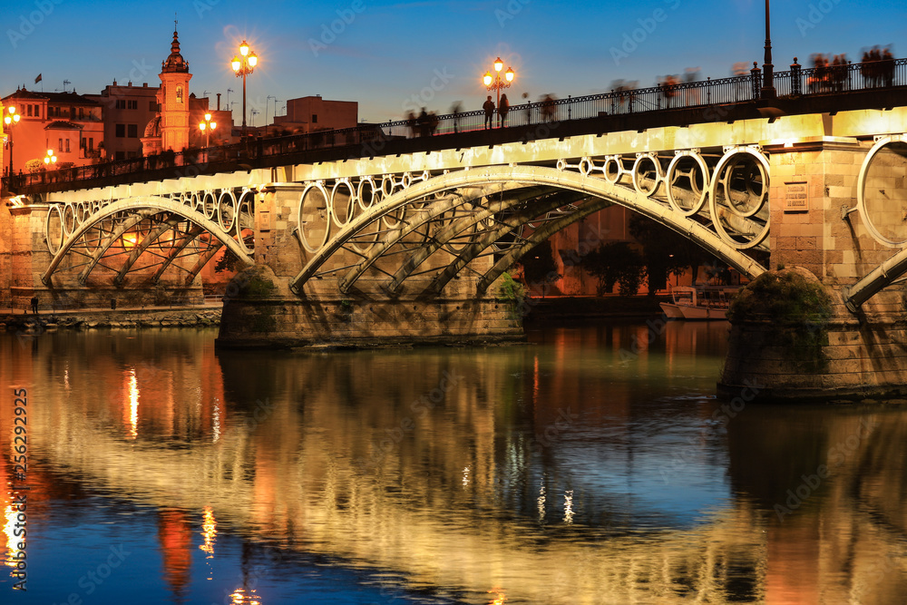 Isabel II bridge or Triana bridge over Guadalquivir river with it’s reflection at twilight, Seville, Andalusia, Spain